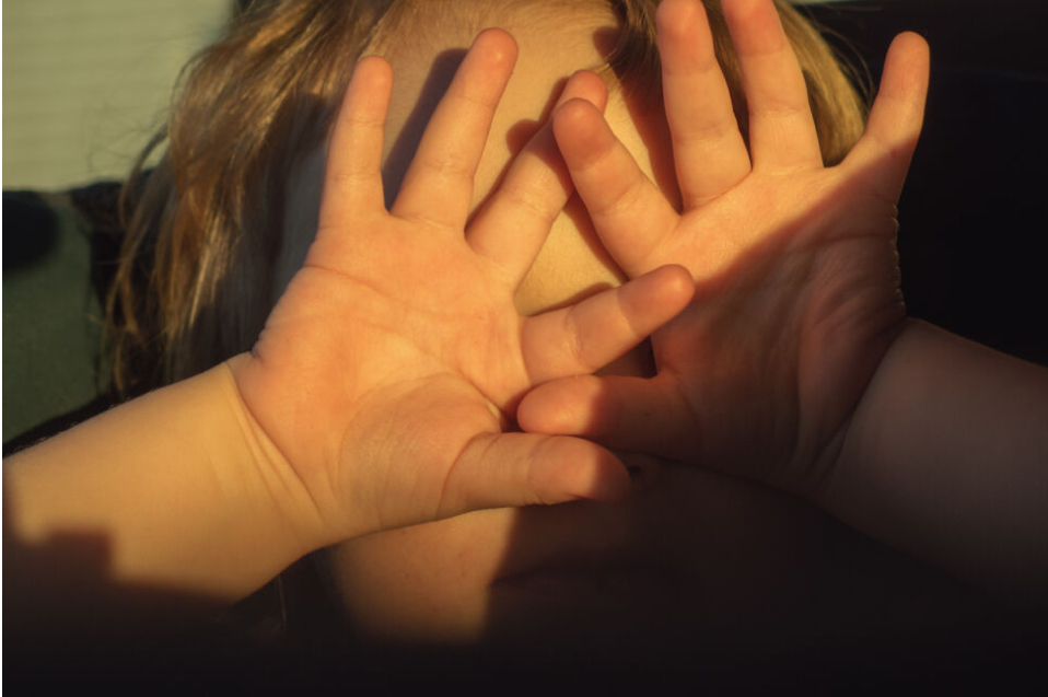 little girl covers her eyes with her hands to keep her out of sight of the sun