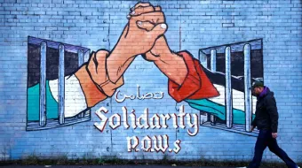 A man walks past a mural in solidarity with Palestinians in the Nationalist area along the International Wall on the Falls Road in Belfast, Northern Ireland
